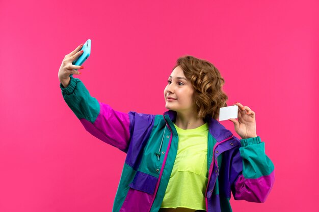 A front view young beautiful lady in acid colored shirt black trousers colorful jacket taking selfie smiling