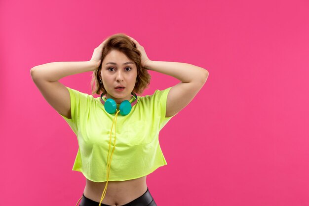 A front view young beautiful lady in acid colored shirt black trousers with blue earphones excited worried