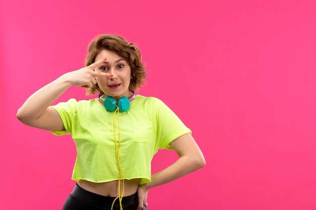 A front view young beautiful lady in acid colored shirt black trousers with blue earphones happy