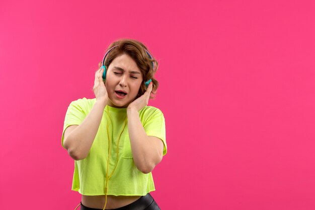 A front view young beautiful lady in acid colored shirt black trousers with blue earphones listening to music singing