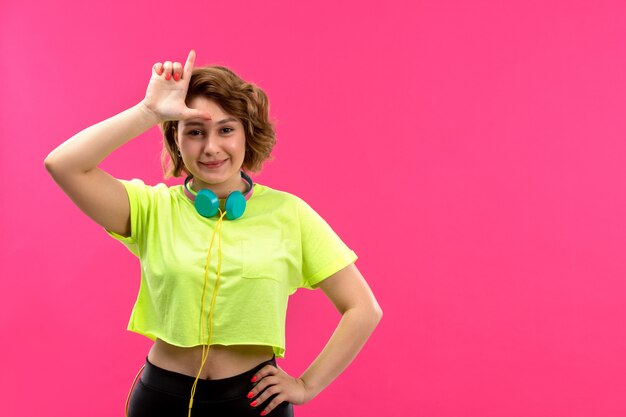 A front view young beautiful lady in acid colored shirt black trousers with blue earphones smiling