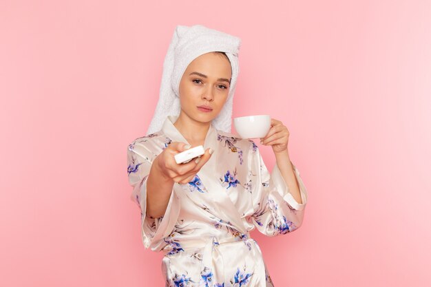 A front view young beautiful lady in bathrobe drinking coffee and switching off air conditioning