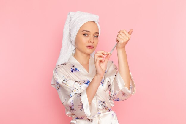 A front view young beautiful lady in bathrobe fixing her nails