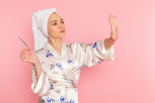 A front view young beautiful lady in bathrobe fixing her nails