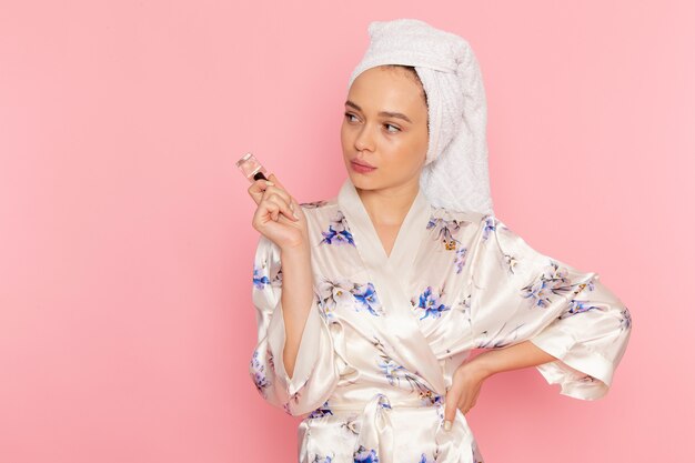 A front view young beautiful lady in bathrobe holding nail polish