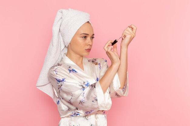 A front view young beautiful lady in bathrobe painting her nails