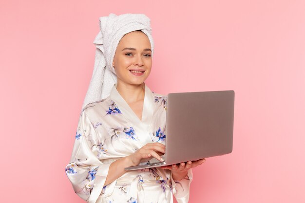 A front view young beautiful lady in bathrobe working with laptop