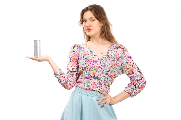 Вид спереди молодая красивая дама в красочном цветочном дизайне рубашки и синей юбке с серебряной банкой с напитком на белом