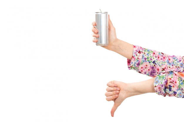 A front view young beautiful lady in colorful flower designed shirt holding silver can showing not good sign on the white