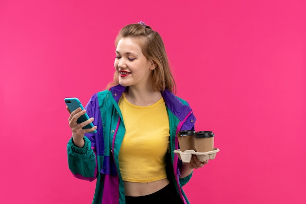 A front view young beautiful lady in colorful jacket orange colored shirt black trousers smiling using her phone with coffee in her hands