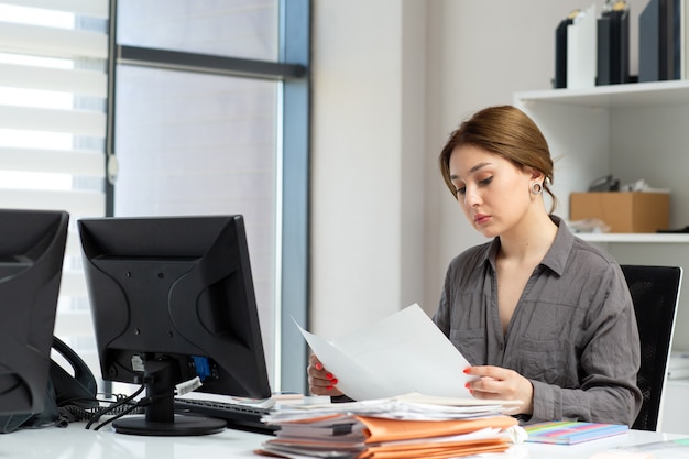 Foto gratuita una giovane bella signora di vista frontale in camicia grigia che lavora con i documenti che si siedono dentro il suo ufficio durante l'attività di lavoro di costruzione di giorno