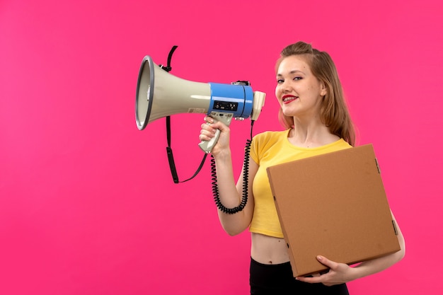 A front view young beautiful lady in orange colored shirt black trousers smiling holding megaphone and package