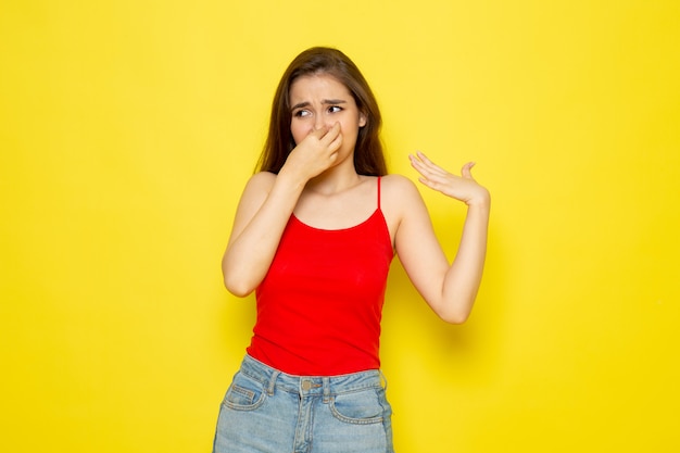 A front view young beautiful lady in red shirt and blue jeans covering her nose