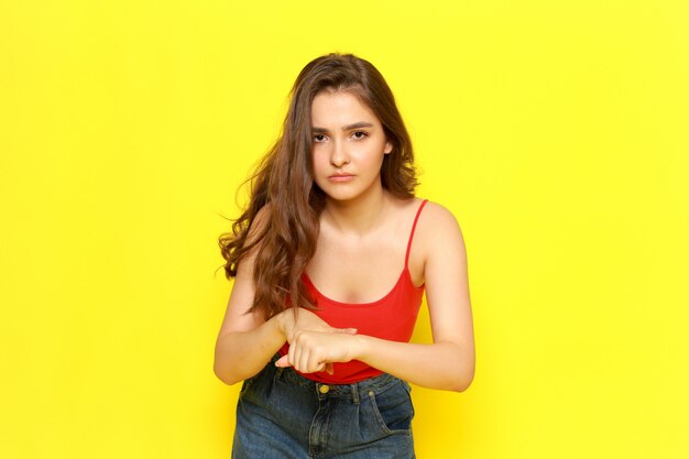 A front view young beautiful lady in red shirt and blue jeans pointing out into her wrist