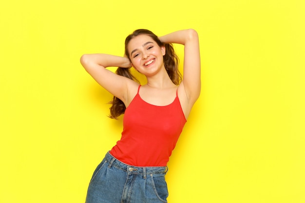 Free photo a front view young beautiful lady in red shirt and blue jeans posing with delighted expression touching her hair