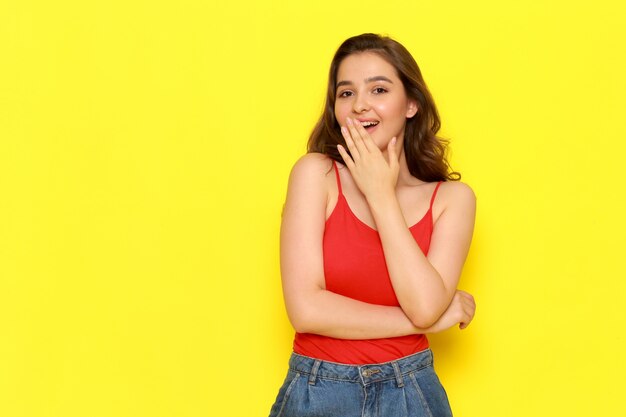 A front view young beautiful lady in red shirt and blue jeans posing with delighted expression