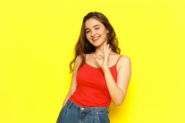 A front view young beautiful lady in red shirt and blue jeans posing with delighted expression