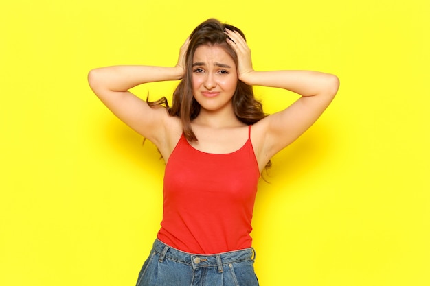 Free photo a front view young beautiful lady in red shirt and blue jeans posing with displeased expression