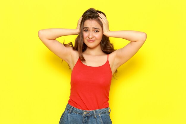 A front view young beautiful lady in red shirt and blue jeans posing with displeased expression