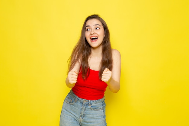 A front view young beautiful lady in red shirt and blue jeans posing with joy