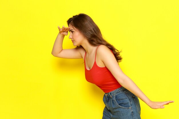 A front view young beautiful lady in red shirt and blue jeans posing with searching expression