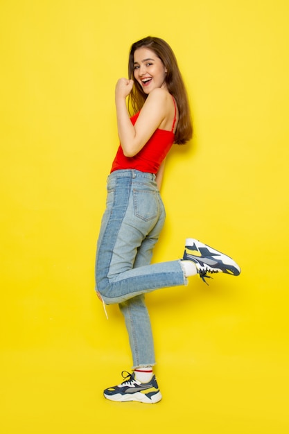 A front view young beautiful lady in red shirt and blue jeans posing with smile