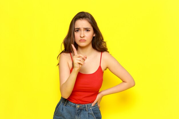A front view young beautiful lady in red shirt and blue jeans posing with threatening expression