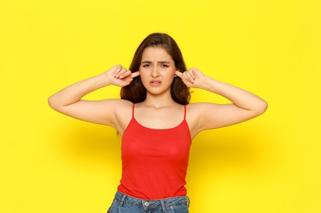 A front view young beautiful lady in red shirt and blue jeans shutting her ears