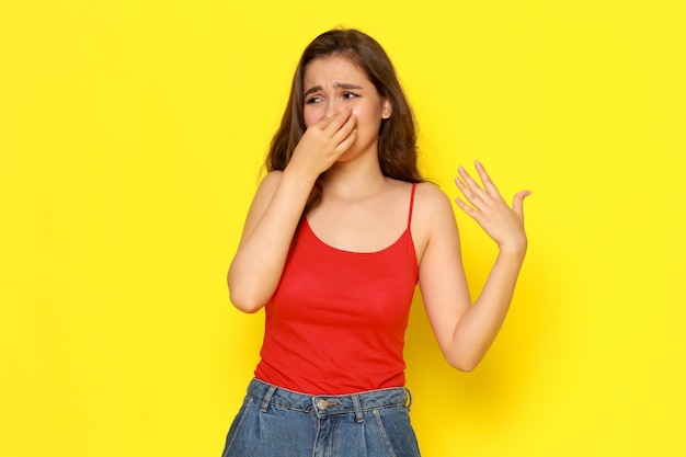 A front view young beautiful lady in red shirt and blue jeans shutting her nose