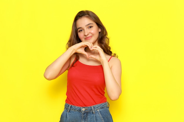 A front view young beautiful lady in red shirt and blue jeans smiling and showing love sign