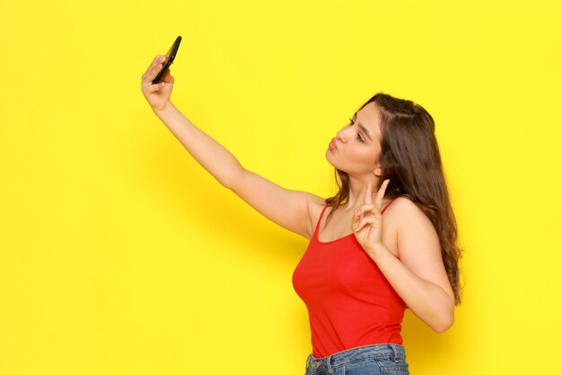 A front view young beautiful lady in red shirt and blue jeans taking a selfie