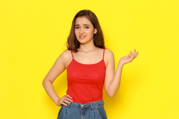 A front view young beautiful lady in red shirt and blue jeans with displeased expression