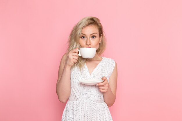 A front view young beautiful lady in white dress drinking a tea