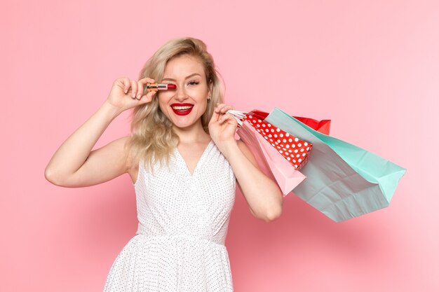 Foto gratuita una giovane donna bella vista frontale in abito bianco tenendo i pacchetti di shopping con il sorriso sul suo viso