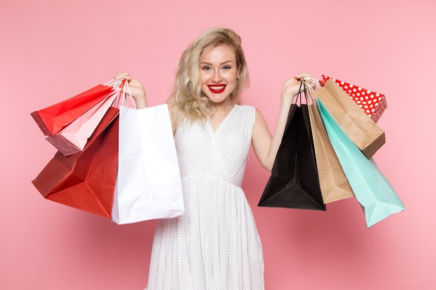 A front view young beautiful lady in white dress holding shopping packages with smile on her face