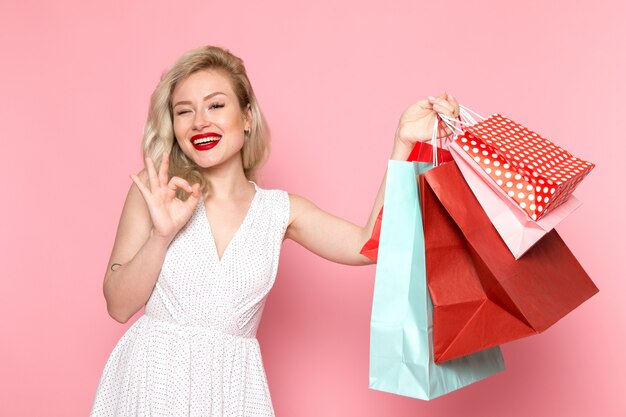 A front view young beautiful lady in white dress holding shopping packages with smile on her face