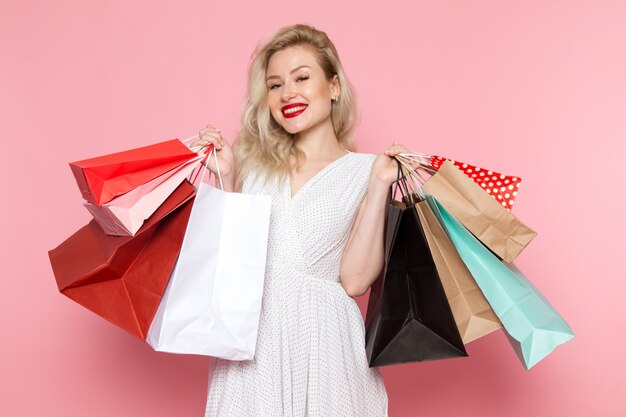 A front view young beautiful lady in white dress holding shopping packages with smile on her face