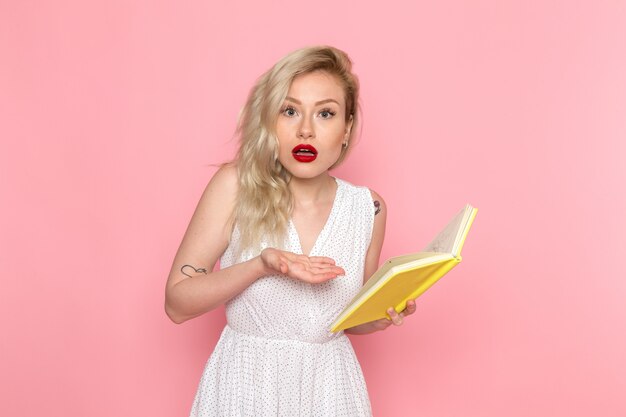 A front view young beautiful lady in white dress reading a copybook with shocked expression