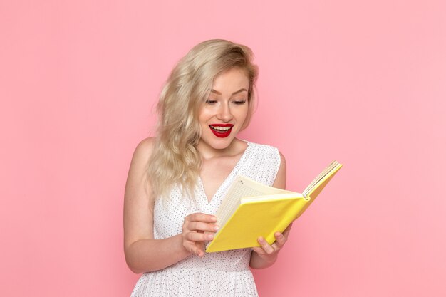 A front view young beautiful lady in white dress reading a copybook with smile on her face