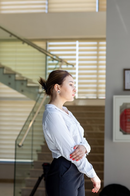 A front view young beautiful lady in white shirt black trousers looking at the distance in the hall waiting during daytime building job activity