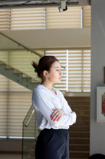 A front view young beautiful lady in white shirt black trousers looking at the distance posing in the hall waiting during daytime building job activity