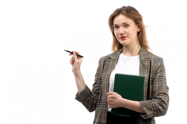 Free photo a front view young beautiful lady in white t-shirt black jeans and coat holding green book and pen smiling on the white