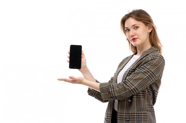 A front view young beautiful lady in white t-shirt black jeans and coat holding showing smartphone on the white