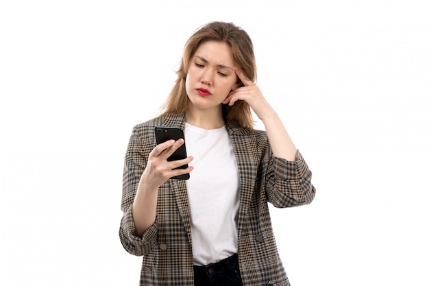 A front view young beautiful lady in white t-shirt black jeans and coat using smartphone on the white