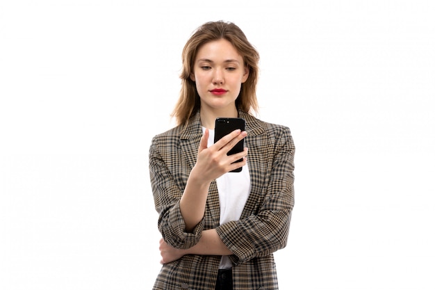 A front view young beautiful lady in white t-shirt black jeans and coat using smartphone on the white