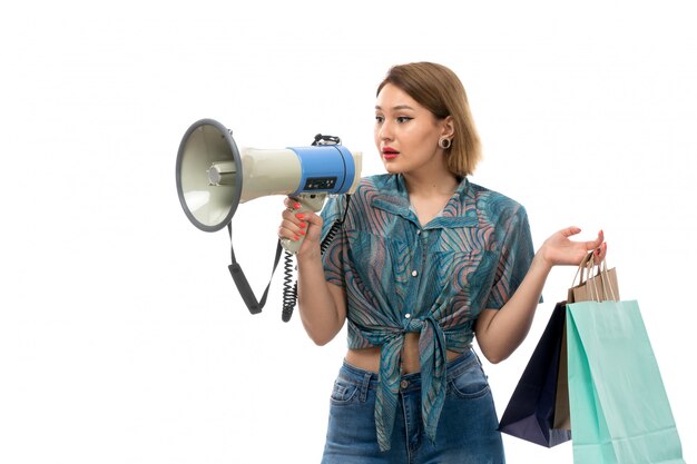 Una giovane donna di vista frontale in blue jeans colorati della blusa che tengono i pacchetti di acquisto facendo uso del megafono