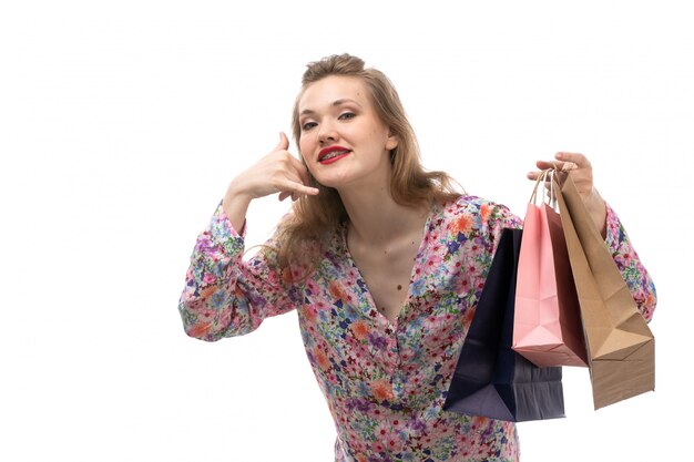 A front view young beautiful woman in flower designed shirt and black trousers holding shopping packages showing phone call gesture