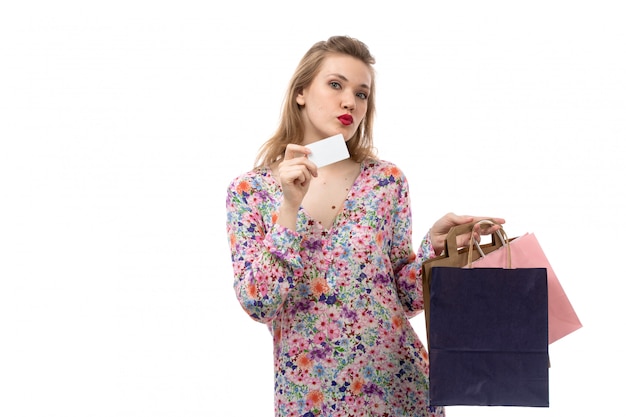 花の正面の若い美しい女性デザインのシャツと白いカードを示すショッピングパッケージを保持している黒いズボン