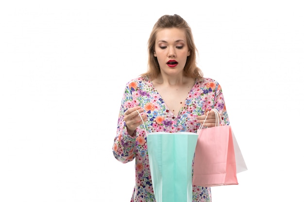 A front view young beautiful woman in flower designed shirt and black trousers holding shopping packages surprised checking