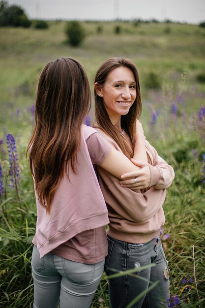 Front view of young brunette girls standing in field with high green grass and lupines and smiling